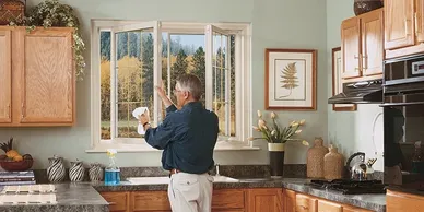 A man is cleaning the window of his kitchen.